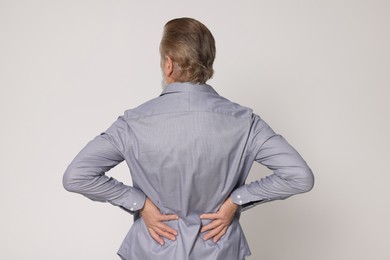 Senior man suffering from pain in back on light grey background. Arthritis symptoms