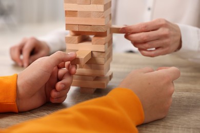 People playing Jenga tower at wooden table indoors, closeup