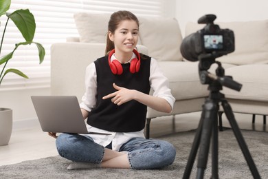 Smiling teenage blogger pointing at laptop while streaming at home