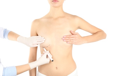 Photo of Doctor drawing marks on patient's breast for cosmetic surgery operation against white background, closeup