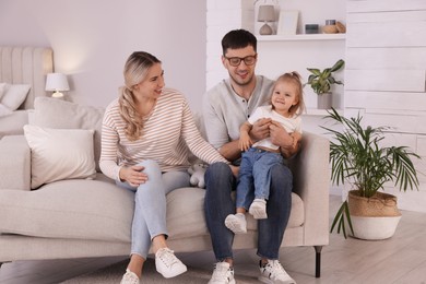 Photo of Family with little daughter spending time together on sofa at home