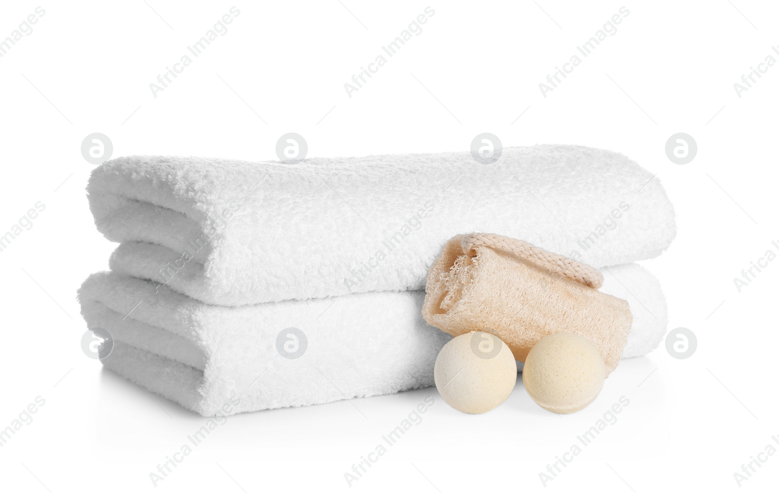 Photo of Stack of clean soft towels, bath bombs and sponge on white background