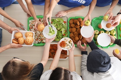 Photo of Volunteers serving food to poor people at table, top view