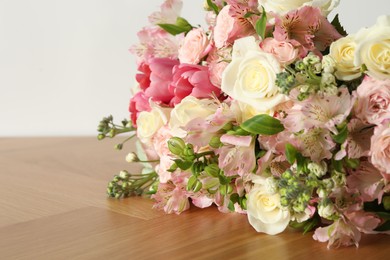 Photo of Beautiful bouquet of fresh flowers on wooden table near white wall, closeup. Space for text