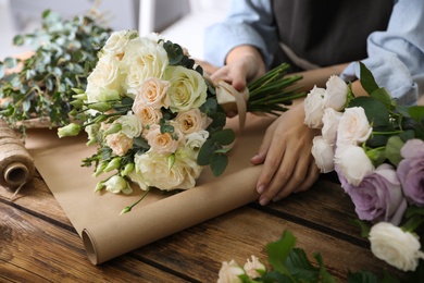 Photo of Florist wrapping beautiful wedding bouquet with paper at wooden table, closeup