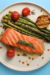 Tasty grilled salmon with tomatoes, asparagus and spices on light blue table, top view