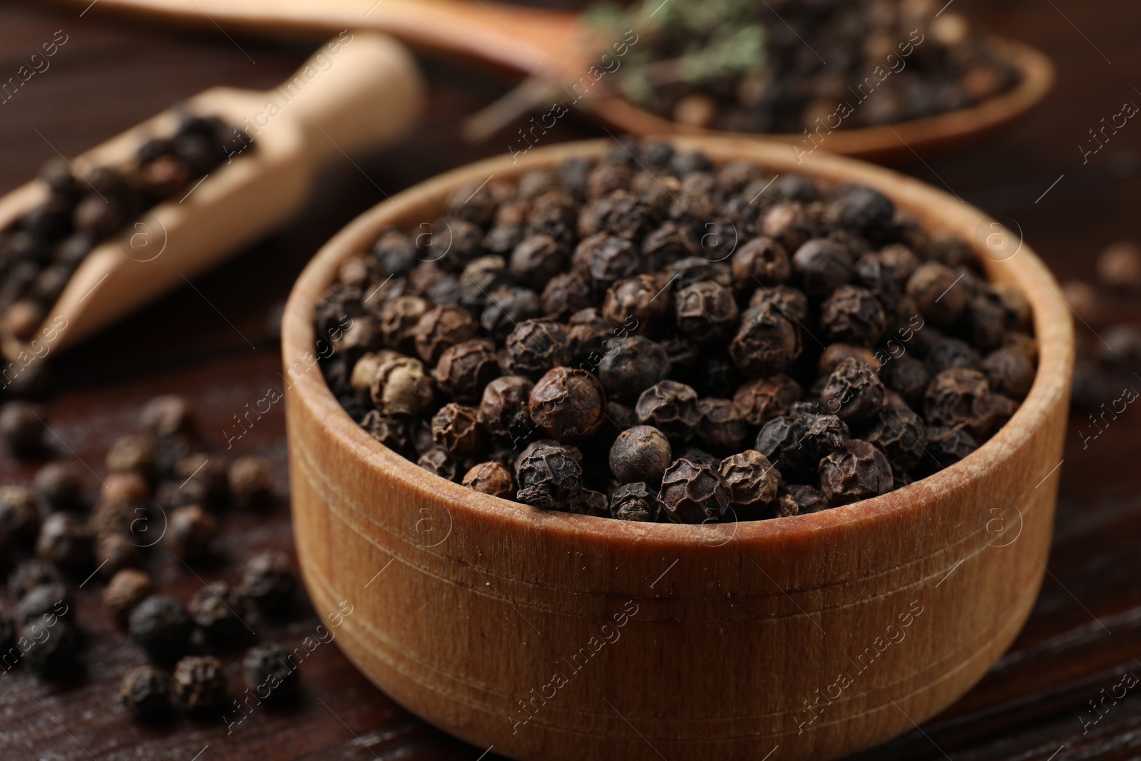 Photo of Aromatic spice. Black pepper in bowl and scoop on wooden table, closeup