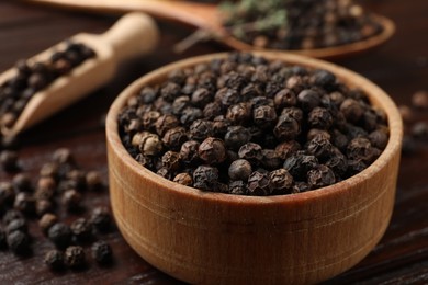 Photo of Aromatic spice. Black pepper in bowl and scoop on wooden table, closeup