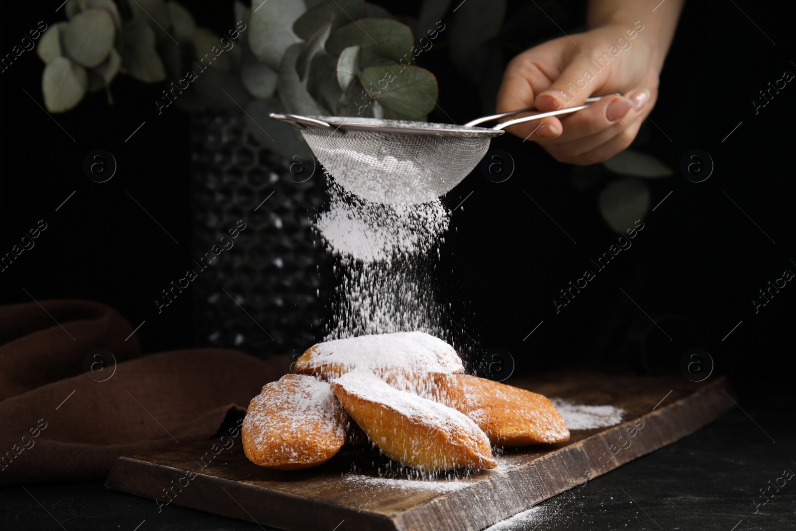 Photo of Woman decorating delicious madeleine cakes with powdered sugar at table, closeup