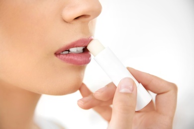 Photo of Young woman applying balm on her lips against light background, closeup