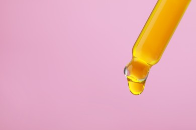 Photo of Dripping yellow facial serum from pipette on pink background, closeup. Space for text