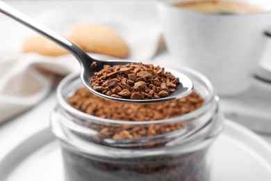 Photo of Instant coffee and spoon above glass jar on table, closeup