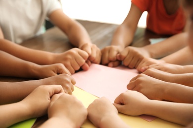 Photo of Little children putting their hands together at table, closeup. Unity concept