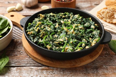 Photo of Tasty spinach dip with eggs in dish served on wooden table, closeup