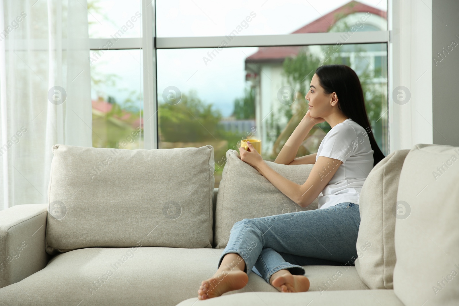 Photo of Young woman with cup of coffee relaxing on sofa at home, space for text