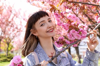 Photo of Beautiful young woman near blossoming sakura tree in park