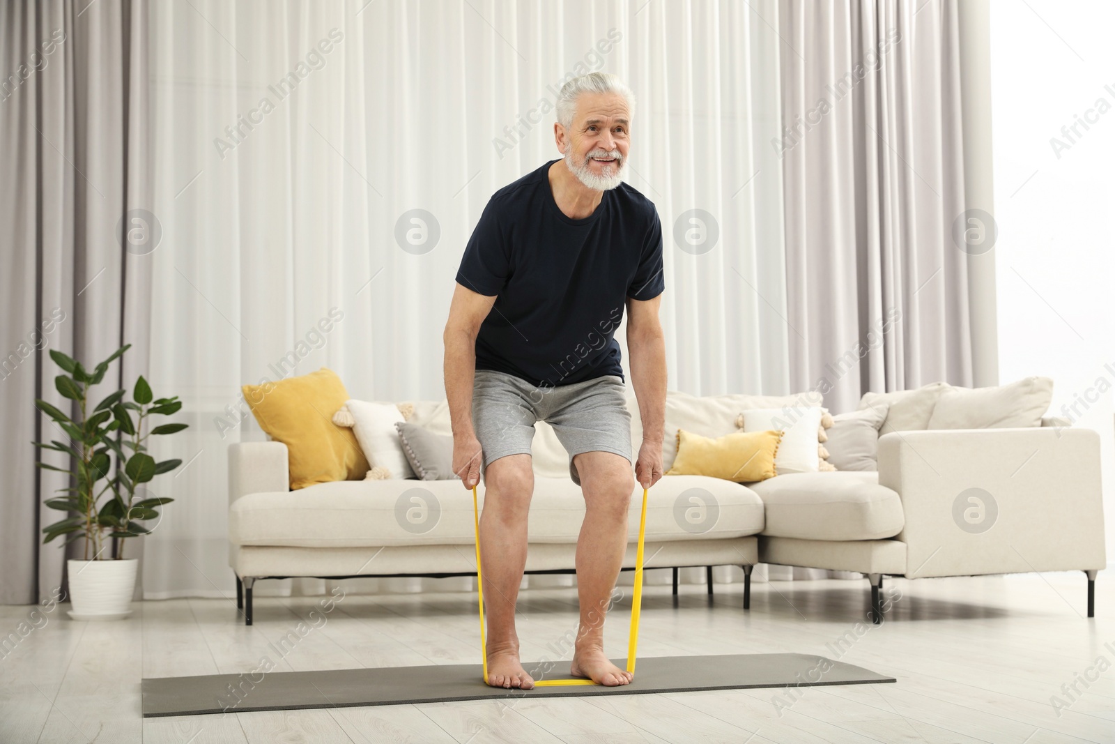 Photo of Senior man doing exercise with fitness elastic band on mat at home