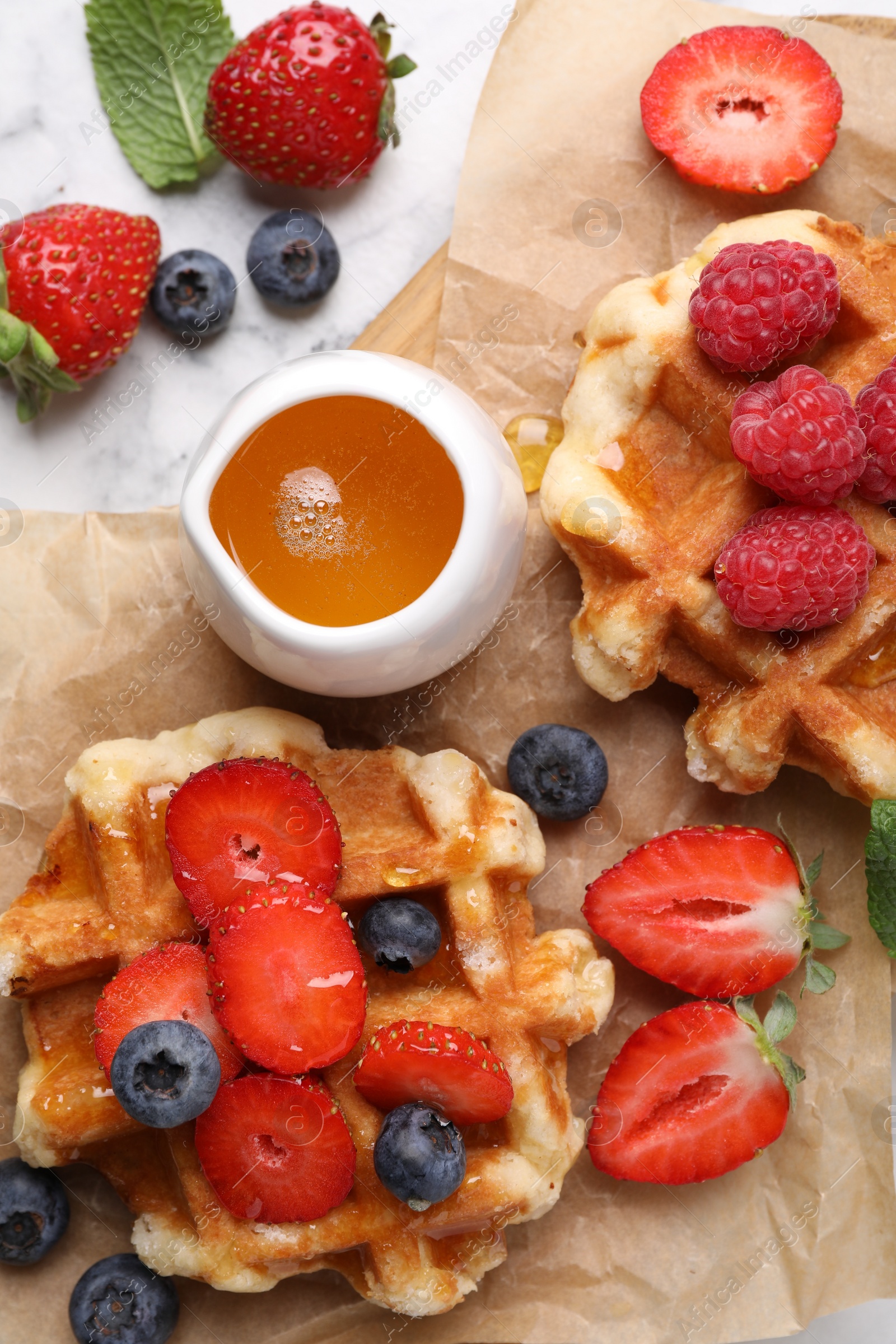 Photo of Delicious Belgian waffles with fresh berries and honey on white marble table, flat lay