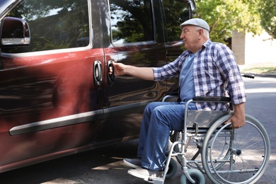 Photo of Senior man in wheelchair opening door of van outdoors
