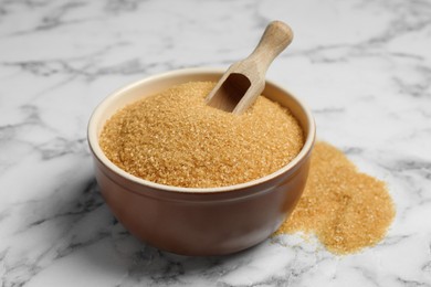Photo of Brown sugar and scoop in bowl on white marble table, closeup