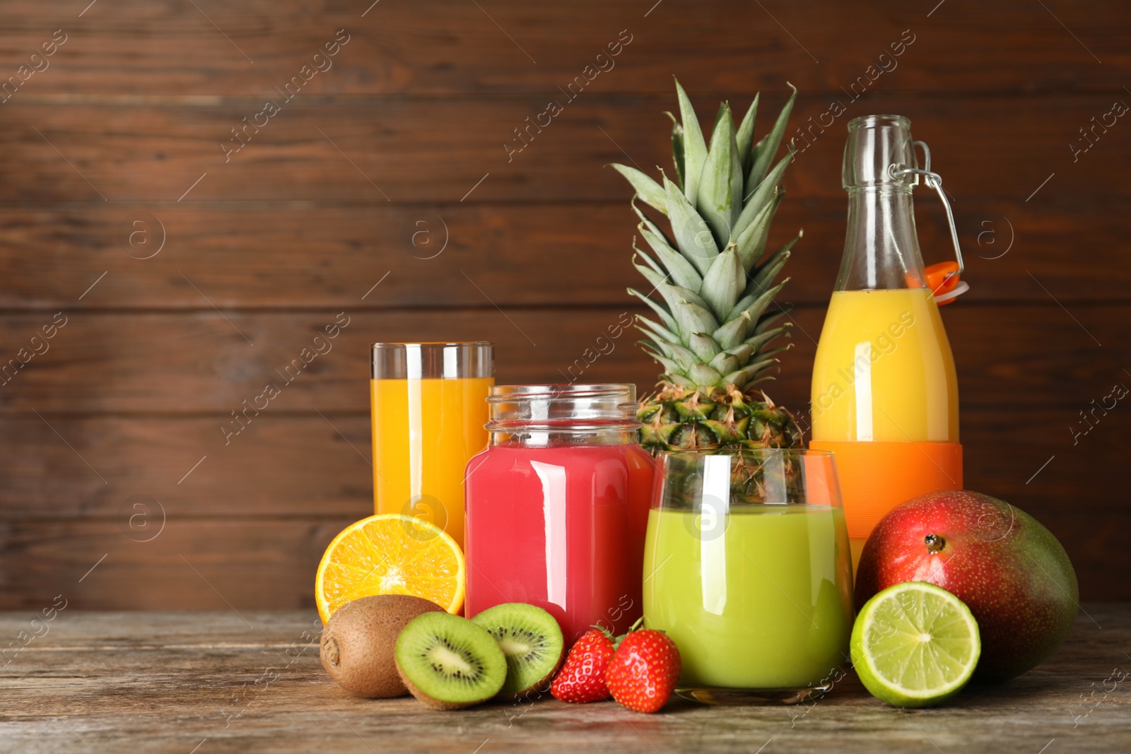 Photo of Glassware with different juices and fresh fruits on wooden background. Space for text