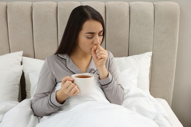 Sick young woman with cup of hot tea in bed