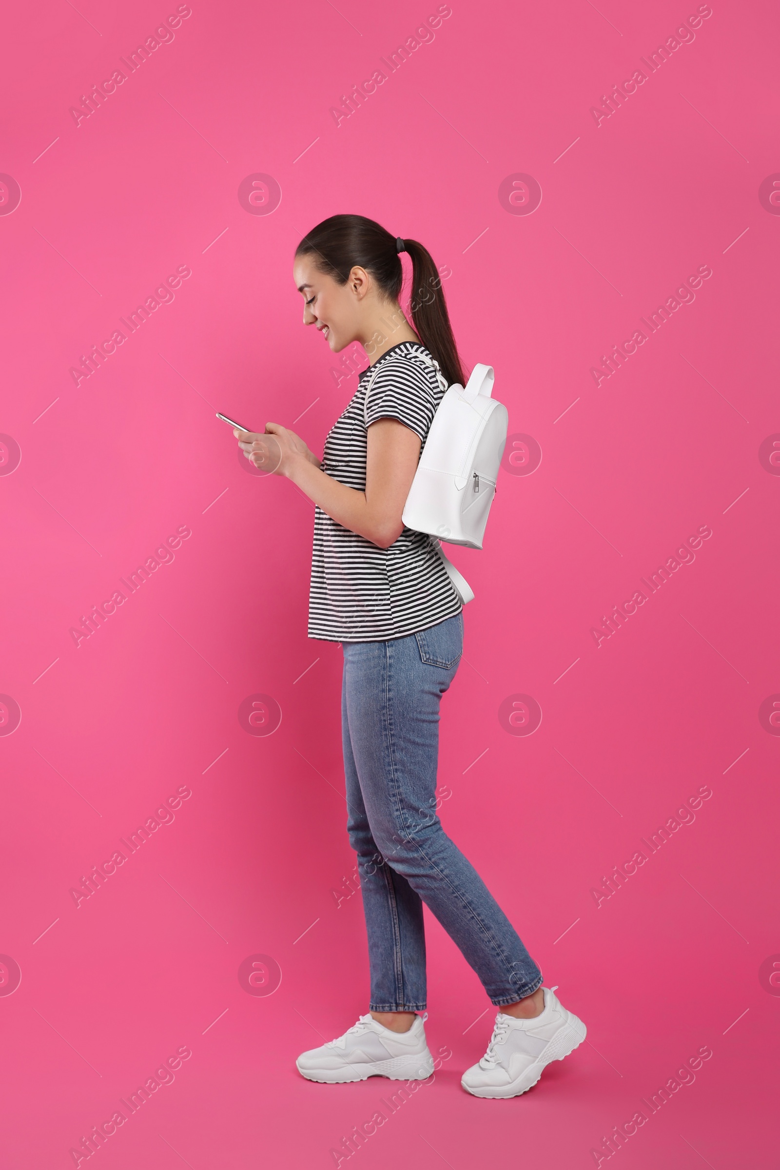 Photo of Beautiful young woman with stylish leather backpack and smartphone on pink background