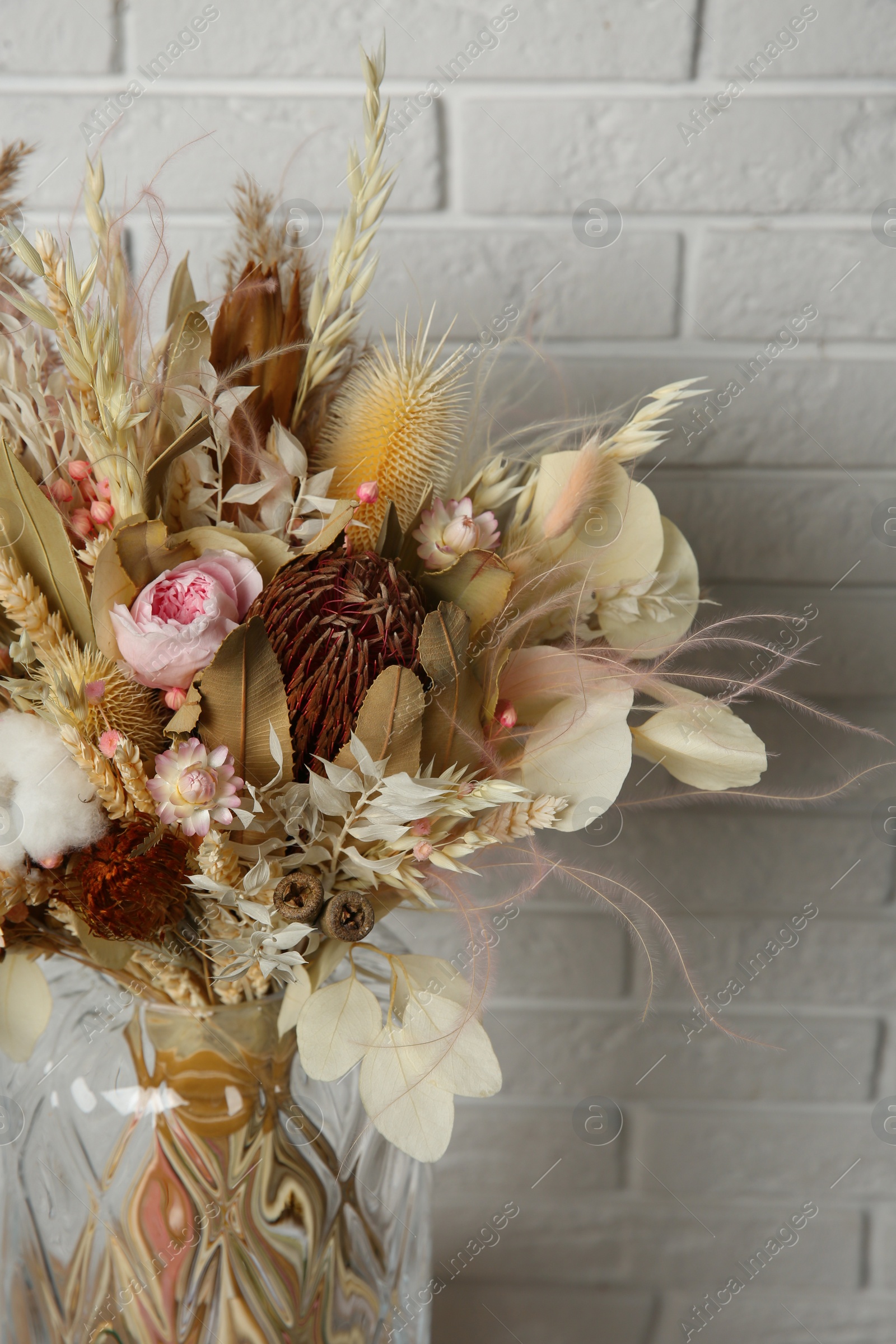 Photo of Beautiful dried flower bouquet in glass vase near white brick wall