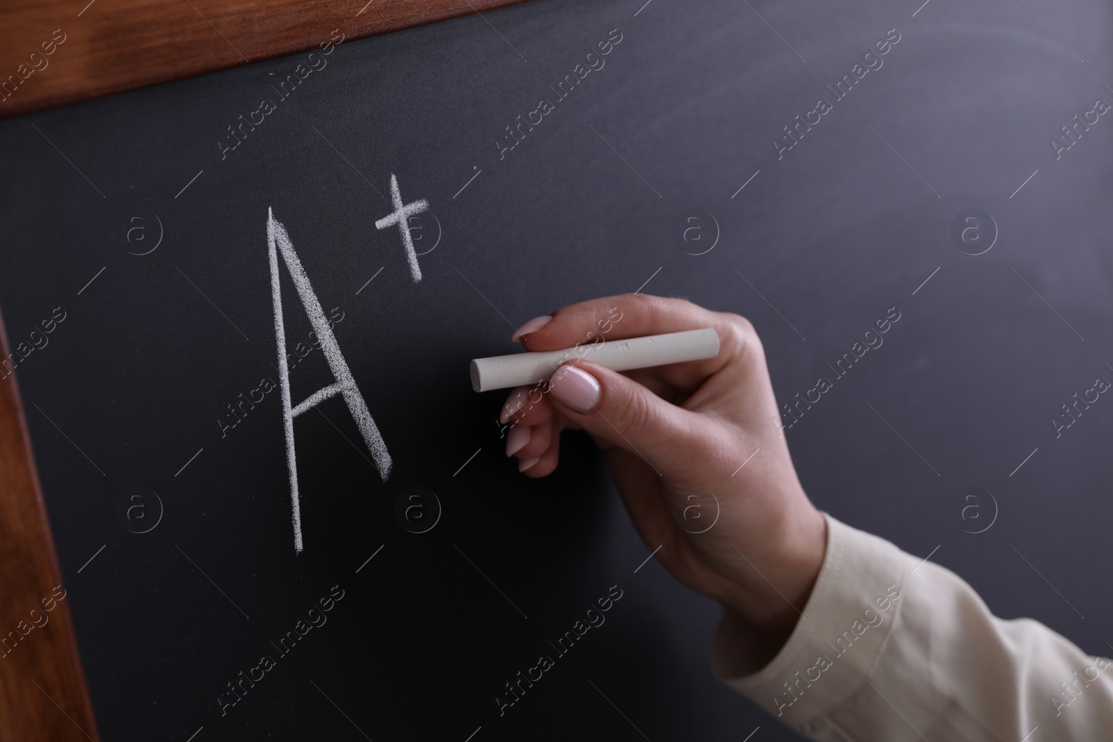 Photo of School grade. Teacher writing letter A and plus symbol with chalk on blackboard, closeup