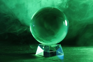 Photo of Crystal ball on table and smoke against dark background. Predictions of future