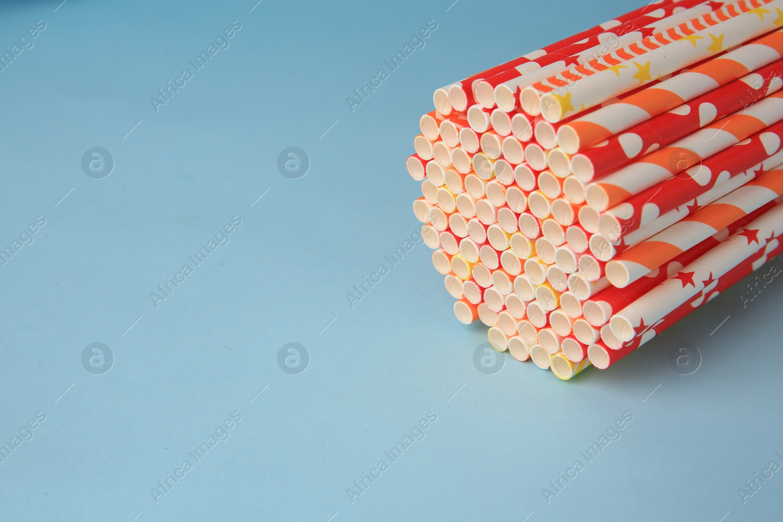 Photo of Colorful paper drinking straws on light blue background, closeup. Space for text
