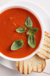 Photo of Delicious tomato cream soup in bowl with pieces of grilled bread on white table, top view