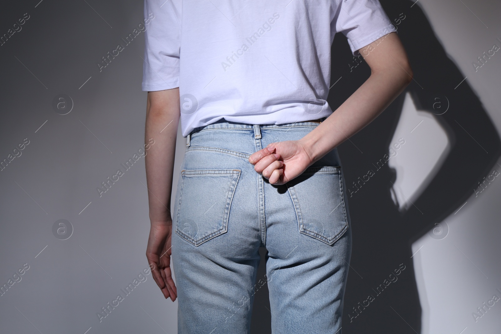 Photo of SOS gesture. Woman showing signal for help behind her back on grey background, back view