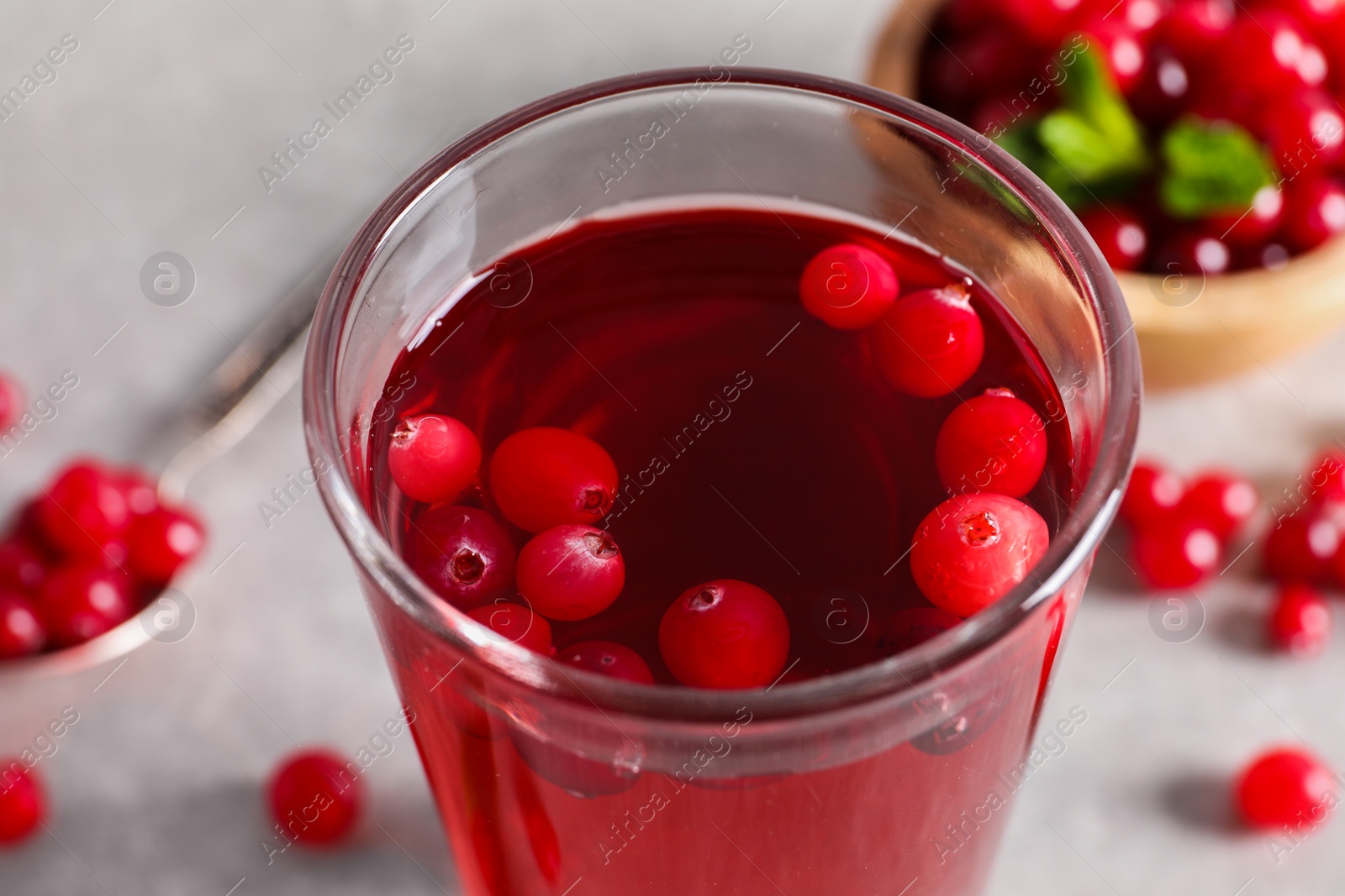 Photo of Tasty cranberry juice in glass and fresh berries on light grey table, closeup
