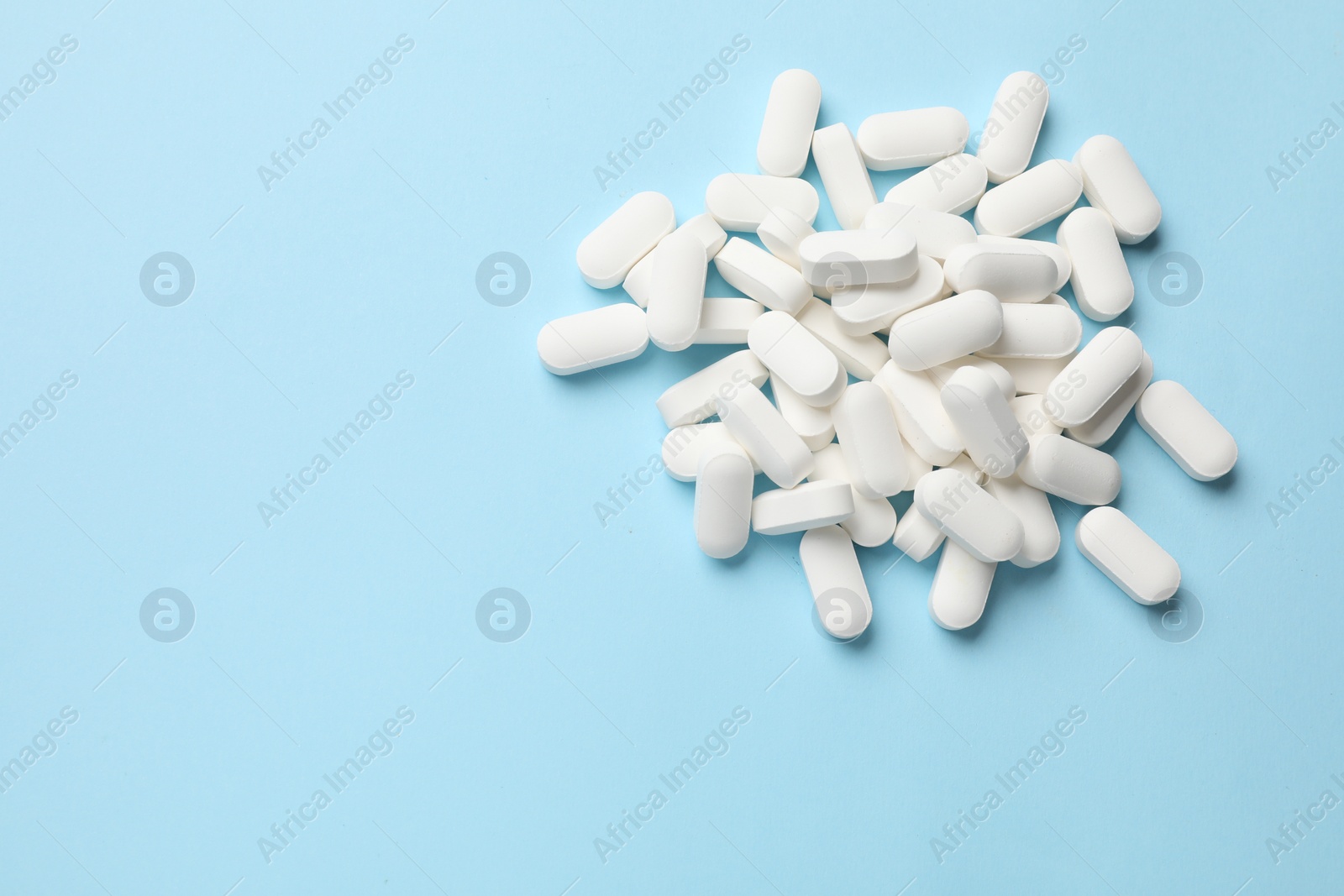 Photo of Vitamin pills on light blue background, top view. Space for text