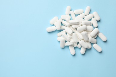 Photo of Vitamin pills on light blue background, top view. Space for text