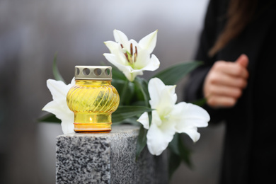 Woman near grey granite tombstone with flowers outdoors, focus on candle. Funeral ceremony