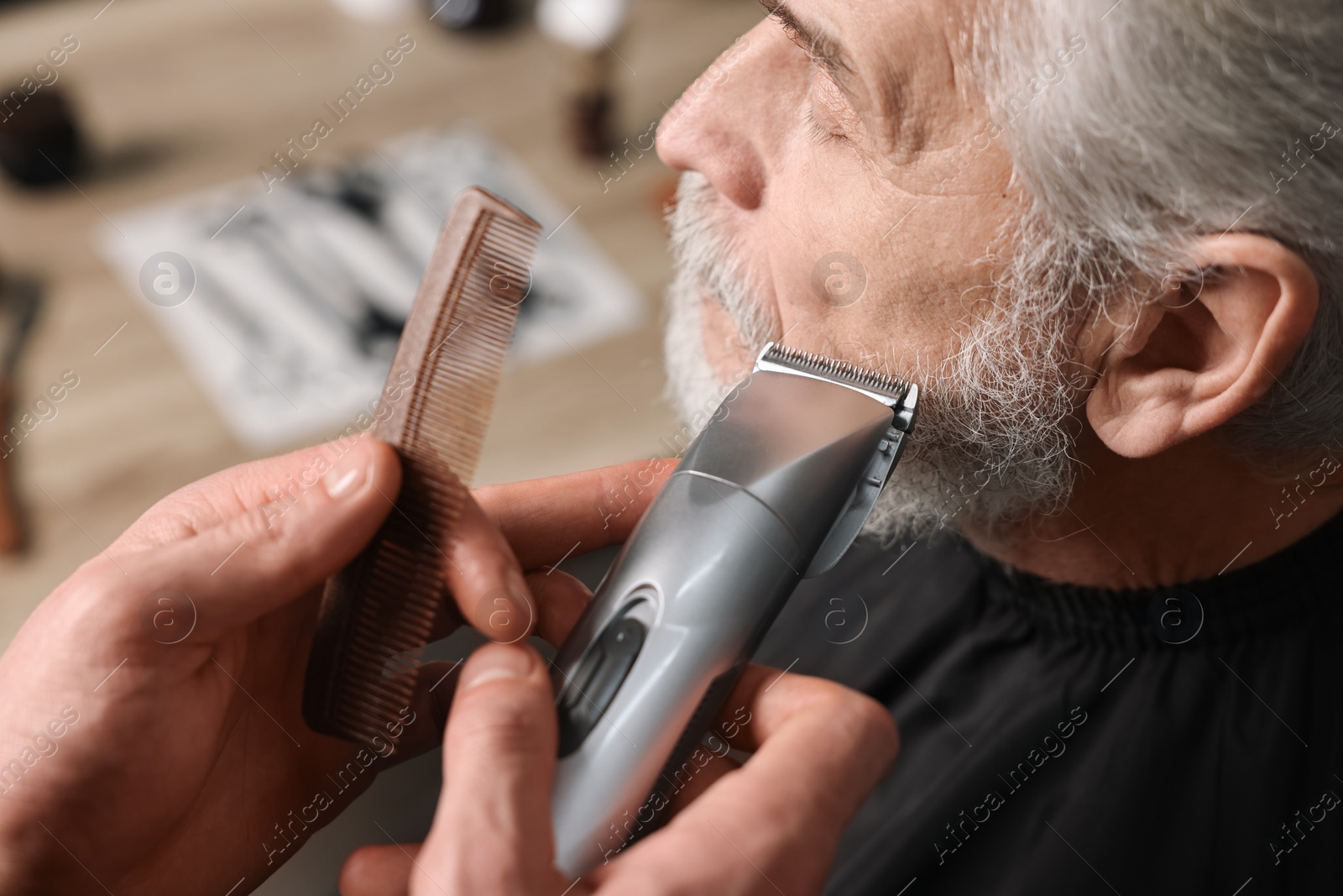 Photo of Professional barber trimming client's beard in barbershop, closeup