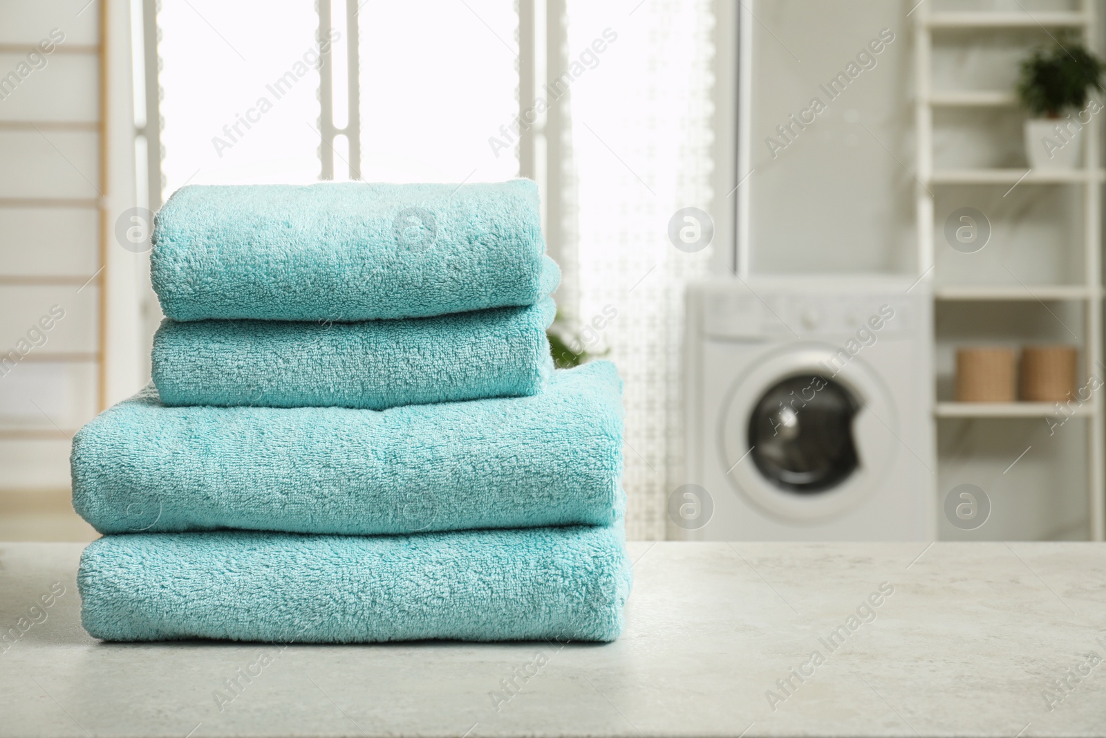 Photo of Stack of clean towels on table in laundry room. Space for text