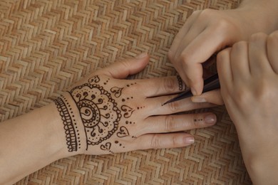 Photo of Master making henna tattoo on hand, top view. Traditional mehndi
