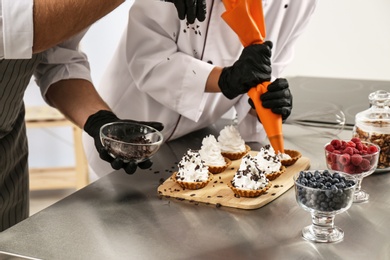 Photo of Pastry chefs preparing desserts at table in kitchen, closeup