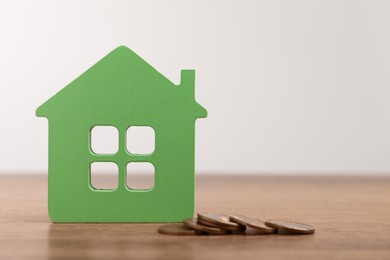 Photo of Mortgage concept. House model and coins on wooden table against white background, space for text