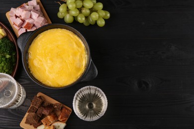 Photo of Fondue pot with melted cheese and different products on black wooden table, flat lay. Space for text