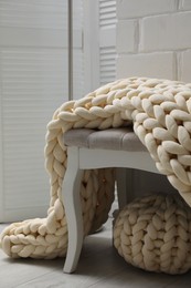 Photo of Indoor bench with soft chunky knit blanket and pouf in room. Interior design