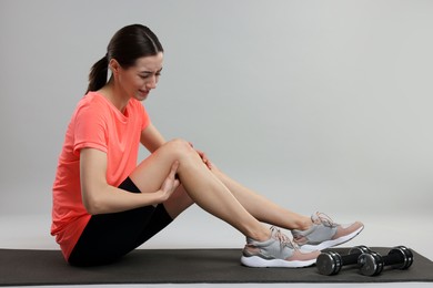 Young woman suffering from leg pain on exercise mat against grey background