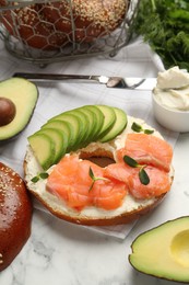 Photo of Delicious bagel with cream cheese, salmon and avocado on white marble table