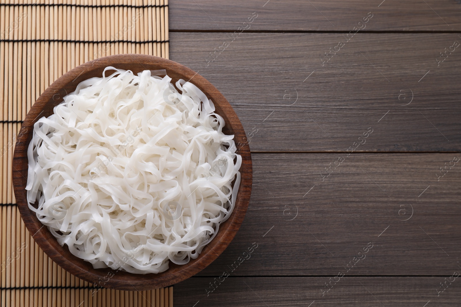 Photo of Bowl of tasty cooked rice noodles on wooden table, top view. Space for text