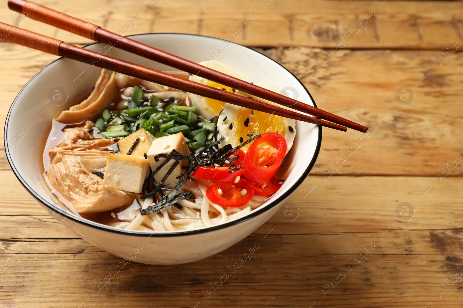 Photo of Noodle soup. Bowl of delicious ramen and chopsticks on wooden table, closeup