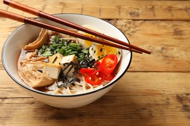 Photo of Noodle soup. Bowl of delicious ramen and chopsticks on wooden table, closeup