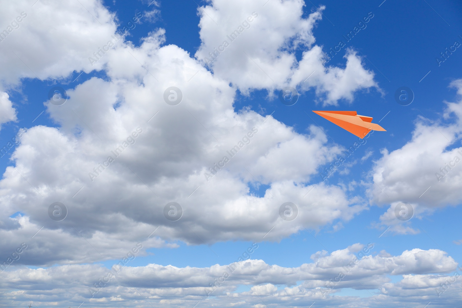 Image of Orange paper plane flying in blue sky with clouds